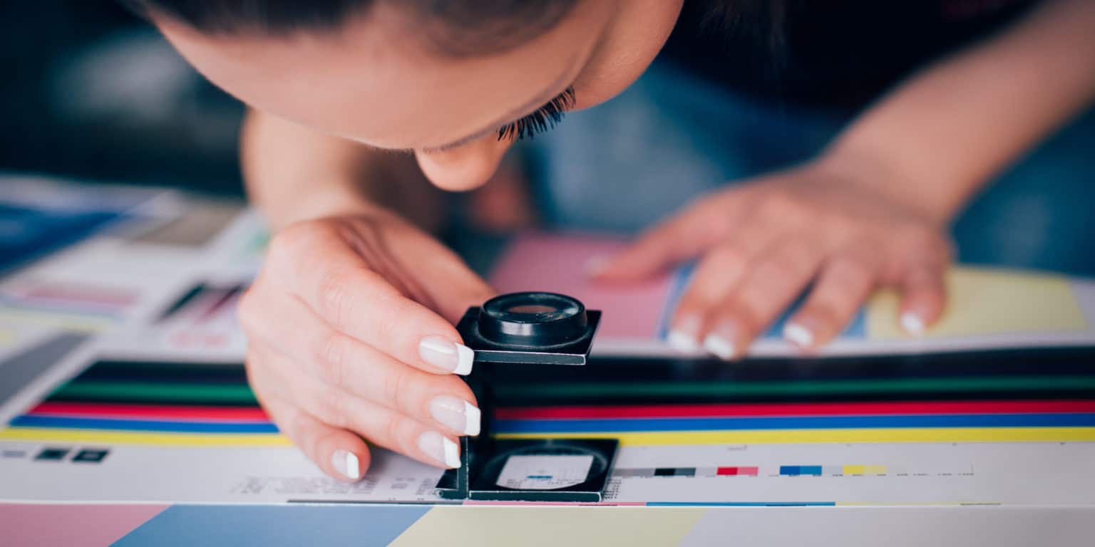 Worker in printing and press centar uses a magnifying glass