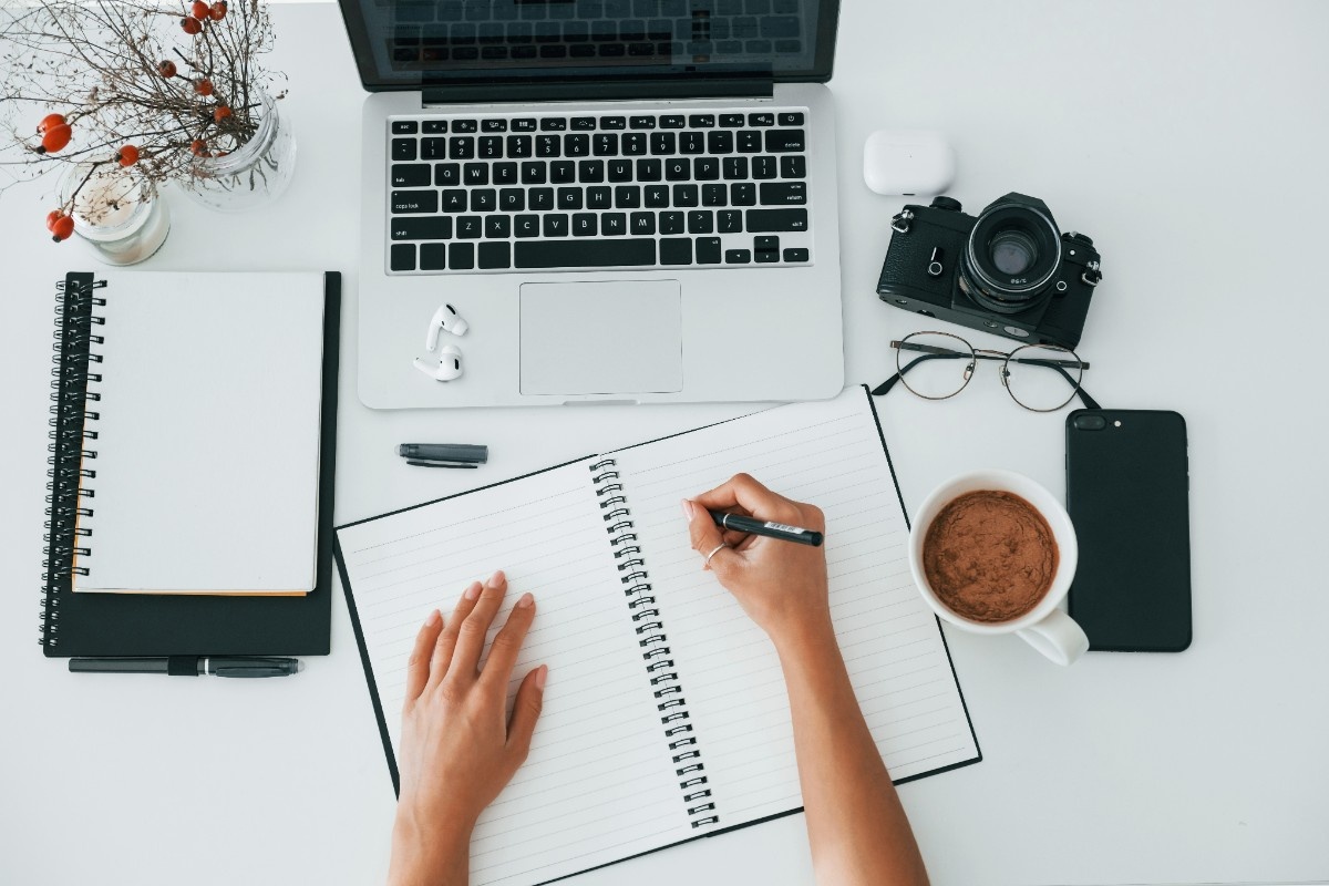 Person writing content on laptop with notes and research materials
