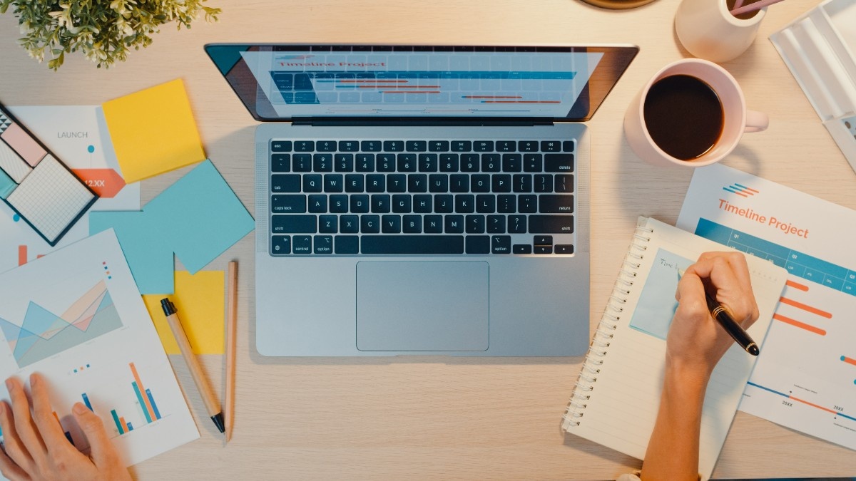 Person writing blog content on laptop with notebook and coffee
