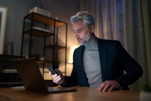 Mature businessman working on laptop at desk indoors in office at night