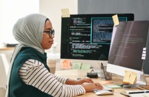 Young Muslim businesswoman in hijab looking at computer screen while typing